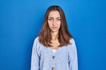 Fototapeta premium Young woman standing over blue background relaxed with serious expression on face. simple and natural looking at the camera.