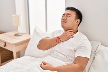 Young chinese man suffering for neck pain sitting on bed at bedroom