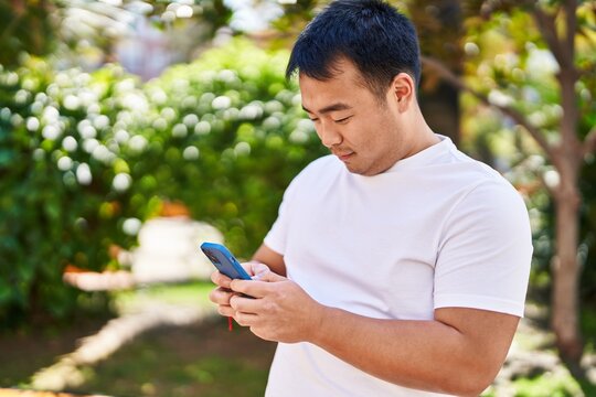 Young chinese man smiling confident using smartphone at park