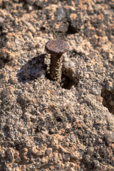 A rusty and old nail or spike driven into a rock. It is a granite rock and you can see a little bit of the nail. Vertical.