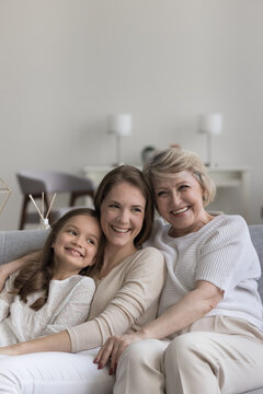 Portrait of three pretty women, multi generational family, female dynasty hugging seated on sofa, laughing, enjoy pleasant pastime together at home, feel happy, enjoy harmonic relationships and bond
