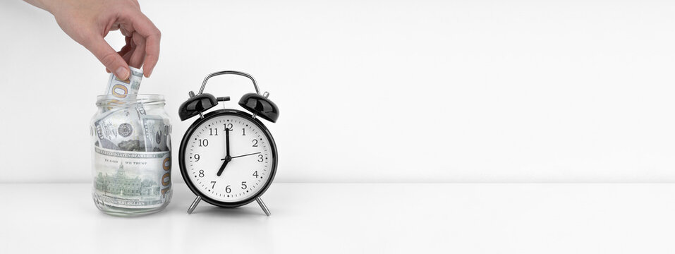 Womans hand put dollar bancnote into a glass jar with alarm clock