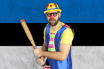 An insecure clown holds a bat in his hands against the background of the flag of Estonia