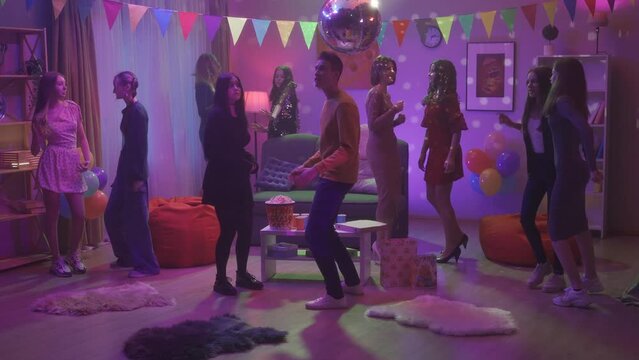 Friends at a party. Children dance in a room with a disco ball to music played from a retro turntable. The girl in black feels awkward, modestly dancing next to the guy. HDR BT2020 HLG Material.
