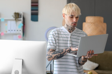 Tattooed graphic designer working with laptop in office