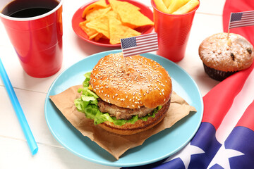 Plate with tasty burger, nachos, muffin and drink on light wooden table. Memorial Day celebration