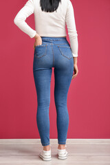 Young woman in stylish jeans near red wall, back view