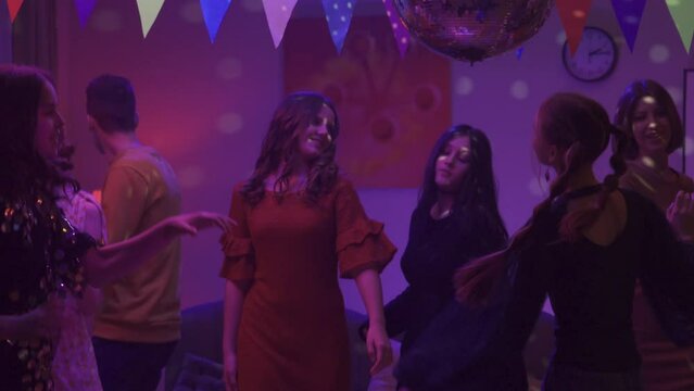 A group of friends are dancing vigorously at a party. The girl in black stands out among everyone with her informality, modesty and bashfulness. Close up. HDR BT2020 HLG Material.