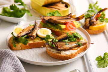 Plate of tasty sandwiches with canned smoked sprats on white wooden background