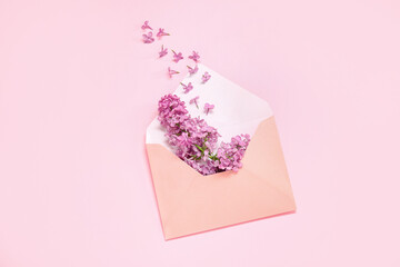 Envelope with beautiful blooming lilac flowers on pink background