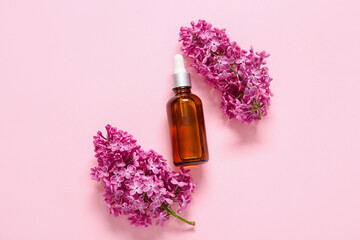 Bottle of essential oil with beautiful lilac flowers on pink background