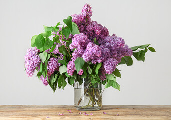 Glass vase of beautiful lilac bouquet on wooden table near white wall