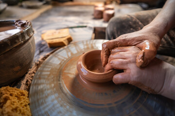 ceramics, workshop, ceramic art concept - close-up of man's hands forming a new vessel, man's fingers working with potter's wheel and raw edge, frontal close-up.