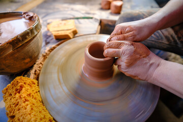 ceramics, workshop, ceramic art concept - close-up of man's hands forming a new vessel, man's fingers working with potter's wheel and raw edge, frontal close-up.