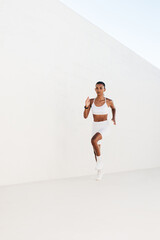 Slim female sprinter running outdoors. Full length of young sportswoman jogging.