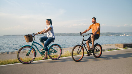 Couple taking pleasure in the ride on beach cruiser bikes, pedaling on a wonderful route near the...