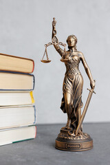 themis goddess of justice statuette on background of books on desktop. symbol of law with scales...