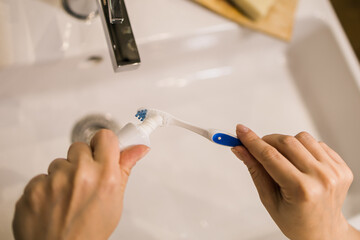 Female hand holding toothbrush with toothpaste applied on it in bathroom. Close up of female hand ready for brushing teeth. Young woman hand holding toothbrush with white tooth paste.