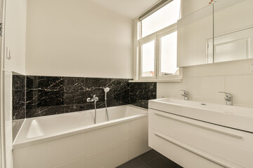a modern bathroom with black and white marble tiles on the walls, tub, sink, and mirror in it