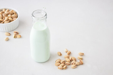 Pistachio milk in a bottle on a gray table next to pistachios. Vegetable milk. Nut milk for vegans