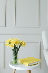 Bouquet of bright yellow daffodils on white wooden table together with yellow book with copy space