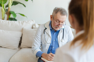 Senior man doctor examining yound woman in doctor office or at home. Girl patient and doctor have...