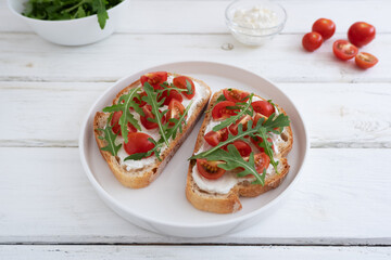 Cherry tomato toast with cream cheese and arugula on wheat bread in a white plate on a light background. Healthy breakfast, Proper nutrition.