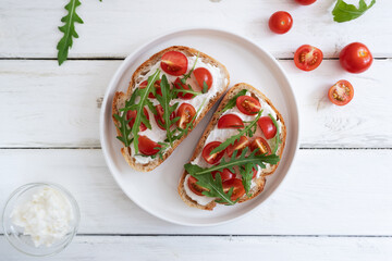 Cherry tomato toast with cream cheese and arugula on wheat bread in a white plate on a light background. Healthy breakfast, Proper nutrition.