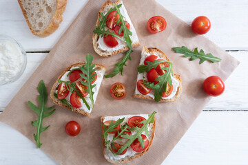 Cherry tomato toast with cream cheese and arugula on wheat bread on craft paper on a light background. Healthy breakfast, Proper nutrition.