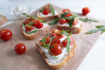 Fototapeta na wymiar Cherry tomato toast with cream cheese and arugula on wheat bread on craft paper on a light background. Healthy breakfast, Proper nutrition.