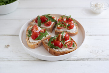 Cherry tomato toast with cream cheese and arugula on wheat bread in a white plate on a light background. Healthy breakfast, Proper nutrition.