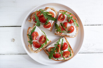 Cherry tomato toast with cream cheese and arugula on wheat bread in a white plate on a light background. Healthy breakfast, Proper nutrition.