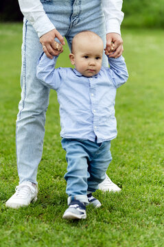 baby learns to walk holding mother's hands. walk with a little boy in nature. lovely one year old boy. child portrait