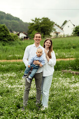 young parents with a smile hold the baby in their arms while on the lawn with flowers. family photo. happy family concept.