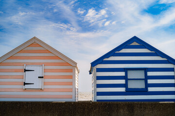 Fototapeta na wymiar Two striped wooden beach huts on a day with blue sky and white clouds.