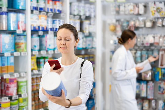 Adult woman in casual clothes looking for baby formula from photo on internet on smartphone in pharmacy