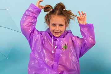 Charming little girl in a purple raincoat. A child dressed for a rainy weather. Isolated on blue background.