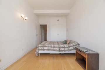 A bedroom with a double bed without a headboard, an old wooden bedside table