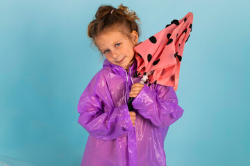 Charming little girl in a purple raincoat holds an umbrella. A child dressed for a rainy weather. Isolated on blue background.