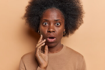 Portrait of stunned stupefied African woman with curly bushy hair stares with omg expression...