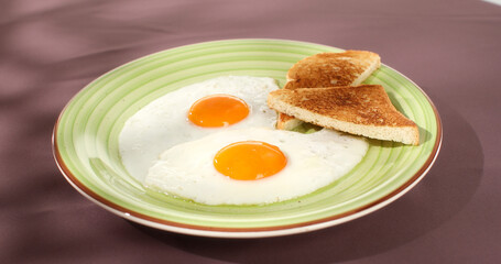 fried eggs with toast on a green plate. close-up. angle view. camera tracking. colored background. traditional breakfast. sunny day.