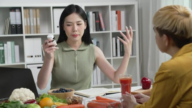 Woman Asian Professional Nutritionist explaining the data on the phone to her client, surrounded by a variety of fruits, nuts, vegetables, and dietary supplements on the table