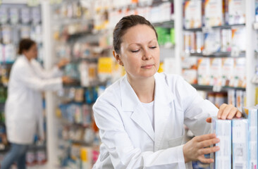 Adult woman pharmacist distributes assortment of goods on counter in pharmacy