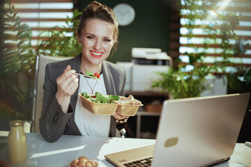 smiling business woman in green office eating salad