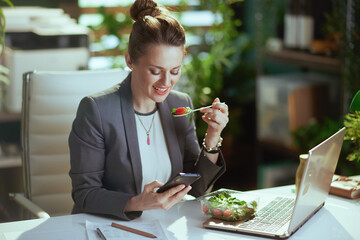 business woman in green office eating salad and using phone