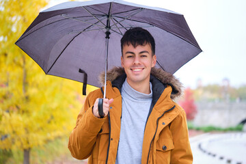 Portrait of a smiling young man holding an umbrella in a rainy autumn day at the street.