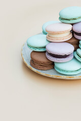 Different pastel colors pastry macarons in plate on a beige vertical background
