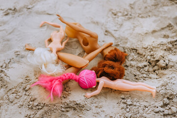 Broken dolls, discarded plastic toys lie in the sand on the playground in the sandbox. Photo,...