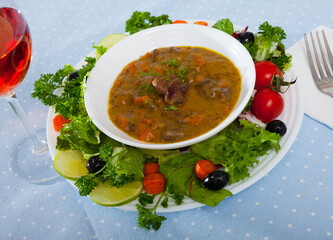 Image of goulash from chicken hearts with vegetables and fresh lettuce served at plate