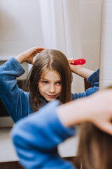 Red-haired teen girl, child combing her hair, taking care of herself, looking in the mirror in the...